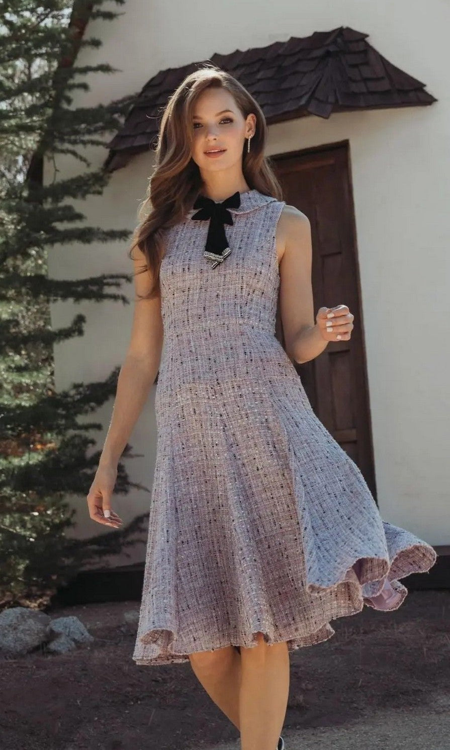 A woman stands outdoors by a white building and trees, wearing the Mac Duggal 56175 Short Wedding Guest Dress in lilac multi.